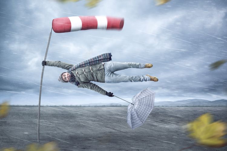 A man getting blown away in a storm, her is trying to hold onto a windsock